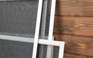 Three rectangular window insect screens with white frames and fine black mesh stacked vertically against a dark wood background.